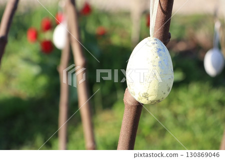 A beautifully decorated Easter egg dangles from a vibrant tree branch, radiating charm and joy 130869046