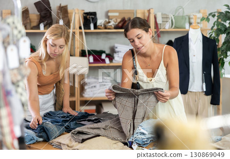 Fashionista girls near showcase examine goods, buying shorts or trousers 130869049