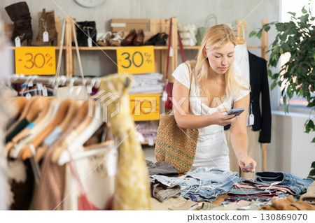 Young female customer scans QR code on trousers or shorts label 130869070