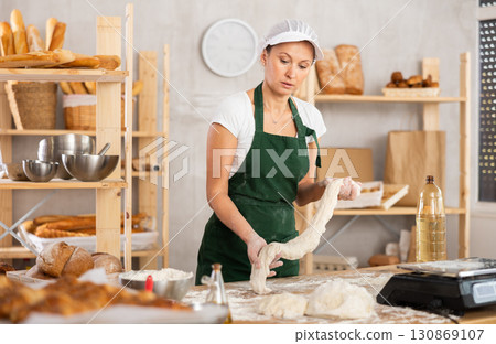 Adult woman baker rolling out raw dough Adult woman baker rolling out raw dough 130869107