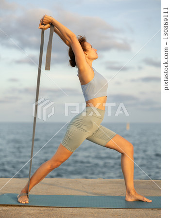 Sporty woman doing yoga with stretch band on seashore Sporty woman doing yoga with stretch band on seashore 130869111