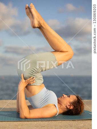 Yoga practice on embankment, female athlete fulfil carry out shoulder stand Yoga practice on embankment, female athlete fulfil carry out shoulder stand 130869203