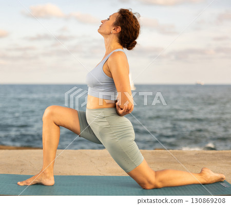 Yoga practice on embankment, female athlete fulfil carry out Anjaneyasana Yoga practice on embankment, female athlete fulfil carry out Anjaneyasana 130869208