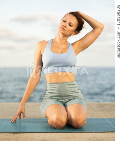 Experienced female trainer doing various exercises to warm up the body before yoga classes on seashore 130869238