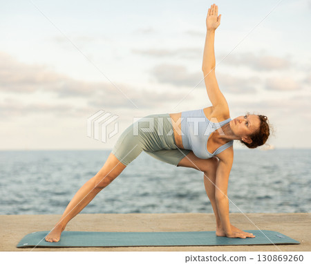 Athletic female yoga practitioner performing Garudasana on beach Athletic female yoga practitioner performing Garudasana on beach 130869260
