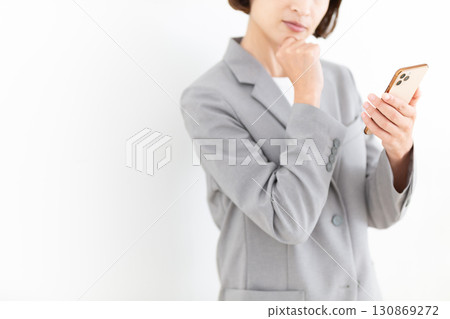 A middle-aged female businesswoman in a suit looking at her smartphone and worrying 130869272