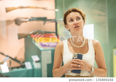 Curious woman examining vintage firearms in military museum 130869288