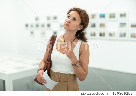 Interested woman studying photos on walls in gallery 130869292