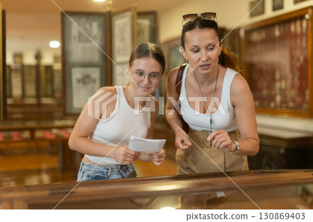 Young woman with teen daughter visitors stands near horizontal glass display case Young woman with teen daughter visitors stands near horizontal glass display case 130869403