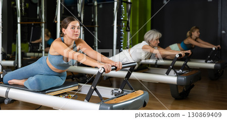 Girl sitting on foldable bed reformer performs exercises, strengthening body and muscles Girl sitting on foldable bed reformer performs exercises, strengthening body and muscles 130869409