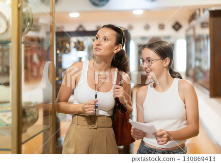 Young woman with teen daughter walk around museum, cookware zone. Young woman with teen daughter walk around museum, cookware zone. 130869413