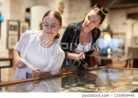 Young woman with teen daughter visitors stands near horizontal glass display case Young woman with teen daughter visitors stands near horizontal glass display case 130869446
