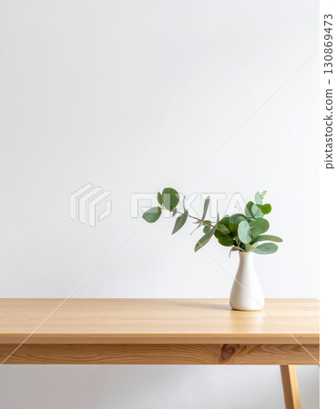 A single green plant in a white vase on a wooden table A single green plant in a white vase on a wooden table 130869473