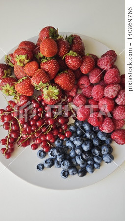 Fresh strawberries, raspberries, blueberries and red currants on a white plate, top view 130869766