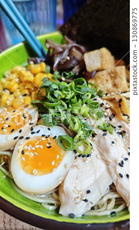 Bowl of ramen with soft-boiled eggs, chicken, corn, tofu and green onions, close-up view 130869775
