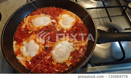 Shakshuka with eggs simmering in tomato sauce in a frying pan on the stove Shakshuka with eggs simmering in tomato sauce in a frying pan on the stove 130869776