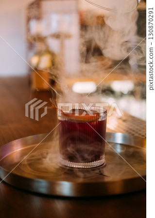 Negroni glass. Smoke drink. Red alcoholic cocktail served with ice cube citrus slice peel. Aromatic refreshing liquor mix on pub counter. 130870291