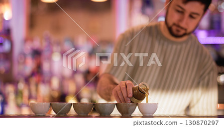 Barman pouring liquid. Asian pub. Bartender filling portioned small ceramic cups for sake. Man serving traditional japanese alcoholic order. 130870297
