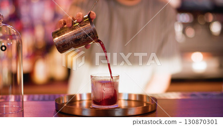 Serving drink. Preparing liquor. Bartender pouring red strained liquid from metal shaker. Professional making refreshing beverage. 130870301