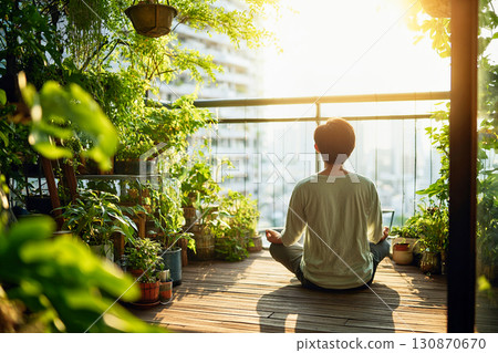 A man meditating in the morning on a balcony surrounded by plants 130870670