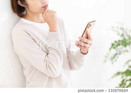 A casual middle-aged female businesswoman thinking while looking at her smartphone 130870684