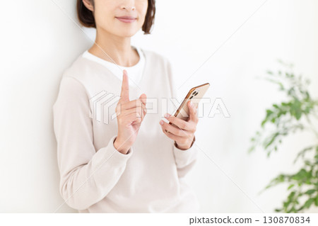 A casual middle-aged female businesswoman holding a smartphone and pointing her index finger up 130870834