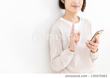 A casual middle-aged female businesswoman holding a smartphone and pointing her index finger up 130870865