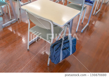 Close-up of desks and chairs in a classroom with school bags hanging from the back, school image 130870880