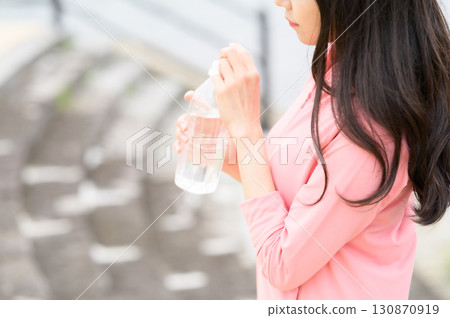 A woman drinking water of a plastic bottle at a park 130870919