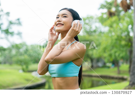 Asian sports woman listening to music on headphones outdoors Asian sports woman listening to music on headphones outdoors 130870927