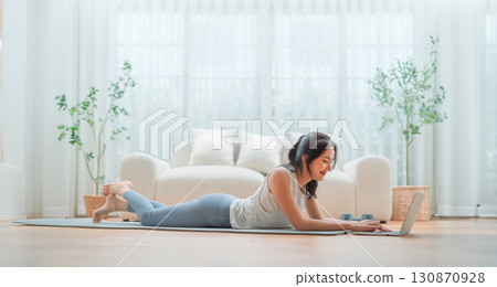 Young Asian woman lying on the floor on yoga mat in front of laptop Young Asian woman lying on the floor on yoga mat in front of laptop 130870928