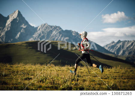 Fitness woman trail runner running in grassland with snow capped mountains in the background 130871263