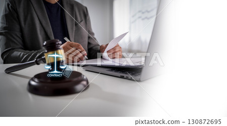 Law and business concept with lawyer reviewing legal documents at office desk, gavel on table, laptop beside, symbolizing corporate legal advice, contract compliance, and justice system. 130872695
