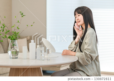 Smiling Asian woman applying foundation, powder, and makeup Smiling Asian woman applying foundation, powder, and makeup 130872811