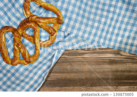 Top view of pretzel loaf on a blue checkered tablecloth or napkin with a wooden table background. Copy space. Concept of Oktoberfest. Bavarian German culture festival decoration symbol 130873005
