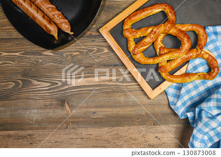 Top view of pretzel loaf and sausage with a blue checkered tablecloth or napkin on a wooden table background. Copy space. Concept of Oktoberfest. Bavarian German culture festival decoration symbol 130873008