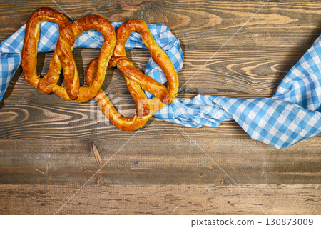 Top view of pretzel loaf on a blue checkered tablecloth or napkin with a wooden table background. Copy space. Concept of Oktoberfest. Bavarian German culture festival decoration symbol 130873009