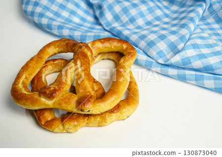 Closeup view of a pretzel loaf with a blue checkered tablecloth or napkin in a white table background. Concept of Oktoberfest. Bavarian German culture festival decoration symbol Closeup view of a pretzel loaf with a blue checkered tablecloth or napkin in a white table background. Concept of Oktoberfest. Bavarian German culture festival decoration symbol 130873040