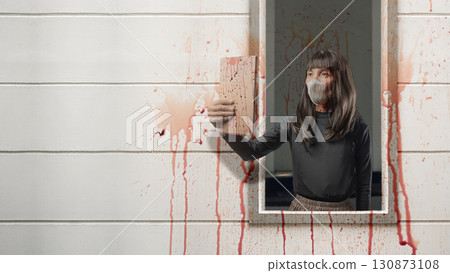 Indonesian southeast asian transgender man dressed as a woman wearing a bloody face mask and using a tablet on wall with splatters of blood background. Concept of Halloween, Sister Hong, or red uncle Indonesian southeast asian transgender man dressed as a woman wearing a bloody face mask and using a tablet on wall with splatters of blood background. Concept of Halloween, Sister Hong, or red uncle 130873108