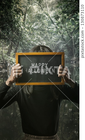 Indonesian southeast asian transgender man dressed as a woman wearing a bloody face mask and showing the text of Happy Halloween on a blackboard. Concept of Halloween, Sister Hong, or red uncle Indonesian southeast asian transgender man dressed as a woman wearing a bloody face mask and showing the text of Happy Halloween on a blackboard. Concept of Halloween, Sister Hong, or red uncle 130873110