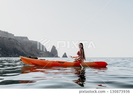 Kayaking, Woman, Ocean - Young woman paddling a kayak on a calm sea with cliffs in the background on a sunny day. Kayaking, Woman, Ocean - Young woman paddling a kayak on a calm sea with cliffs in the background on a sunny day. 130873936