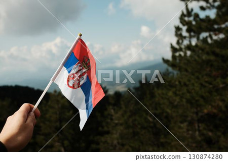 Hand holding Serbian flag with mountain landscape in Divcibare, Serbia. Symbol of national pride and scenic travel 130874280