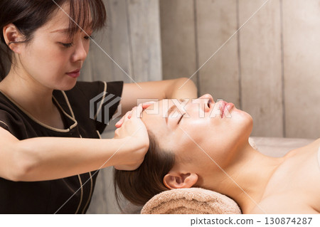 年輕的亞洲美容師正在做頭部按摩。 年輕的亞洲美容師正在做頭部按摩。 130874287