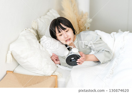 年輕的亞洲女性看到鬧鐘時感到驚訝和驚訝（睡過頭、遲到、睡過頭） 130874620
