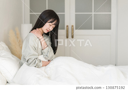A young woman suffers from stiff shoulders due to bedding and pillows that don't fit her (stiff neck, pain, sleep quality, bedding, doesn't fit) 130875192