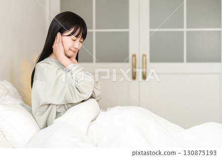 A young Asian woman covering her ears from noise while sleeping in bed (noise trouble, sleep disturbance, sleep disorder) A young Asian woman covering her ears from noise while sleeping in bed (noise trouble, sleep disturbance, sleep disorder) 130875193