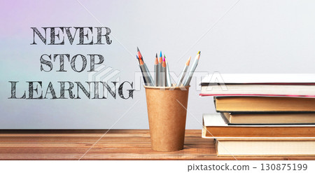 Never stop learning. A pencil holder with pencils sits on a table with a stack of books Never stop learning. A pencil holder with pencils sits on a table with a stack of books 130875199