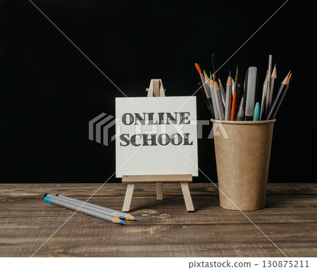 Wooden desk with a sign that says Online School and a cup of pencils 130875211