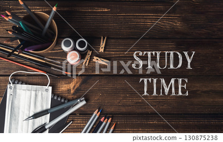 A wooden table with a bowl of pencils, a bottle, and a pair of scissors 130875238