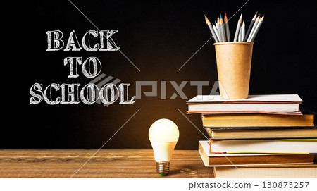 A stack of books and a pencil holder sit on a table with the words Back to School written in chalk A stack of books and a pencil holder sit on a table with the words Back to School written in chalk 130875257